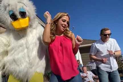 A duck mascot, and young woman and man dancing on outdoor deck 